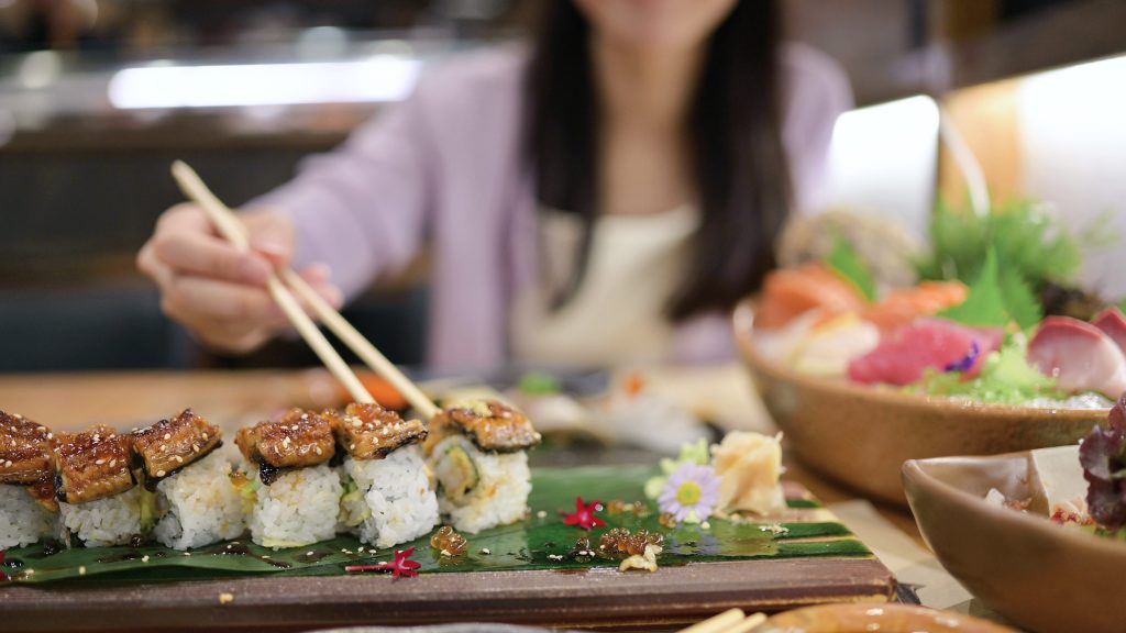 Young asian women eating delicious Unagi Sushi with chopsticks at restaurant.